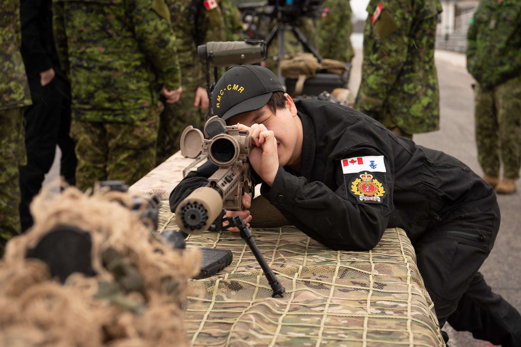 An NCdt looking trough a sniper rifle during a career weekend activity on campus.